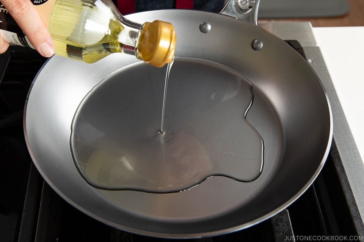 Golden vegetable oil being poured into a non-stick frying pan for Japanese cooking.