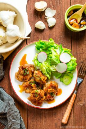 A white plate containing teriyaki pork balls and green salad.