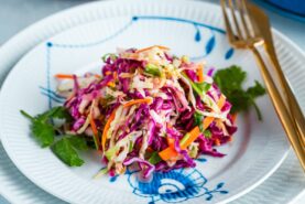 Asian Coleslaw with Sesame Dressing on a white plate along with gold fork and knife.