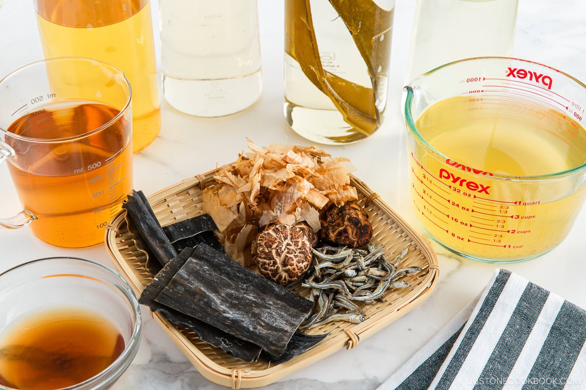 Kombu, Shiitake mushrooms, Katsuobushi, and Iriko are&nbsp;on a bamboo tray, beside cups of dashi. stock.