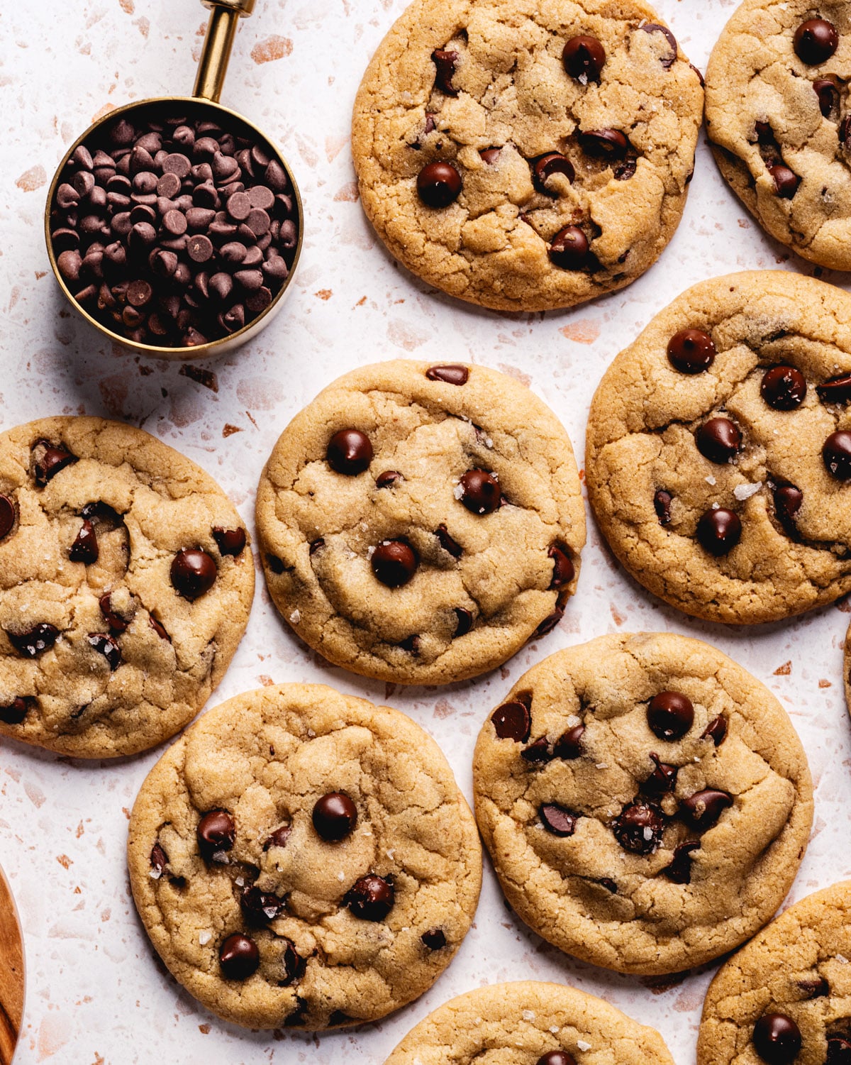 Eggless Chocolate Chip Cookies sprinkled with sea salt and a measuring cup of chocolate chips sitting next to them