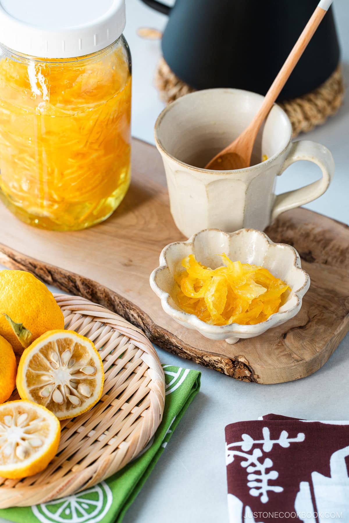 Yuzu cha (citron tea) in a large mason jar, white ceramic cup, and a small dish, and yuzu fruits are placed in a bamboo basket.
