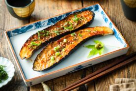 A rectangular plate containing Miso Glazed Eggplant garnished with yuzu kosho paste on a green maple leaf on the side.