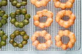 Copycat Pon de Ring donuts, hot from the fryer and still glistening with sugar and matcha glaze, cooling on a wire rack.