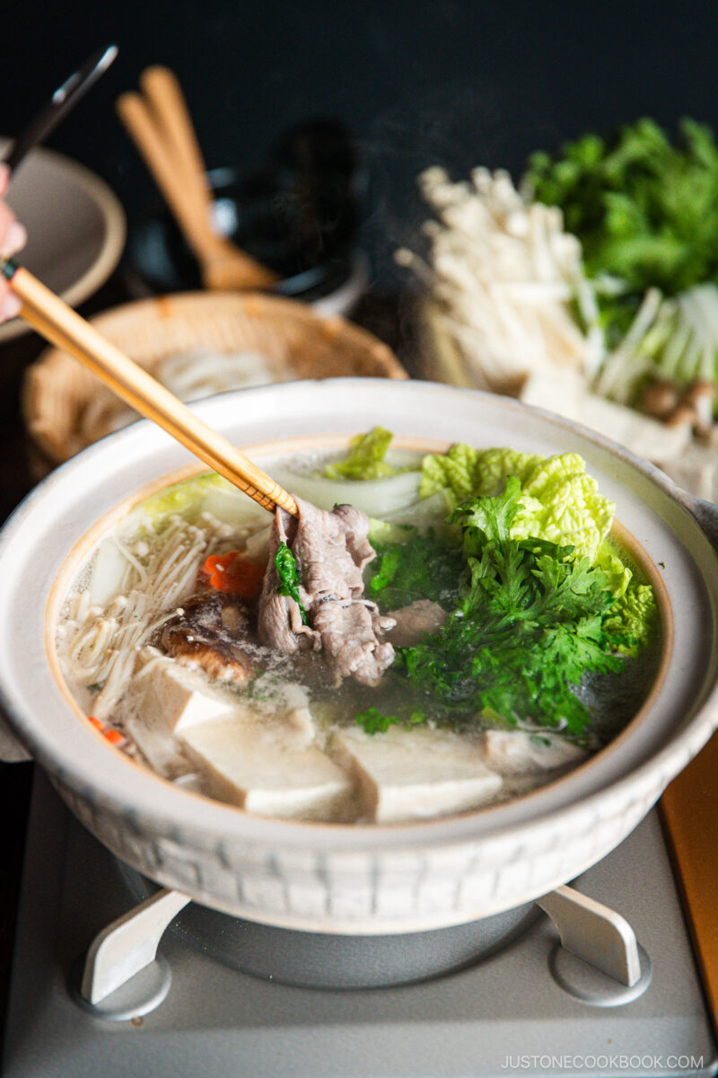 Thinly sliced beef is being cooked in the hot pot along with vegetables and tofu in a donabe, Japnaese hot pot.