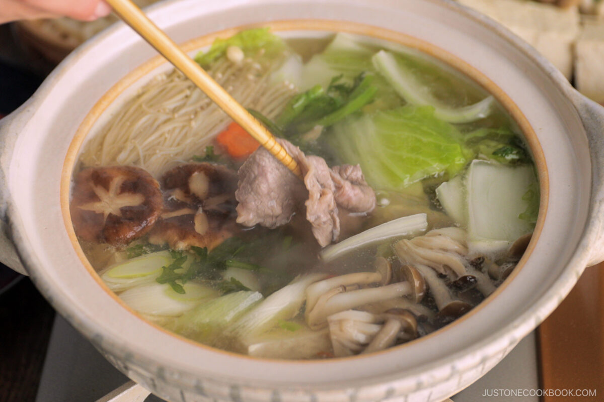 Thinly sliced beef is being cooked in the hot pot along with vegetables and tofu in a donabe, Japnaese hot pot.