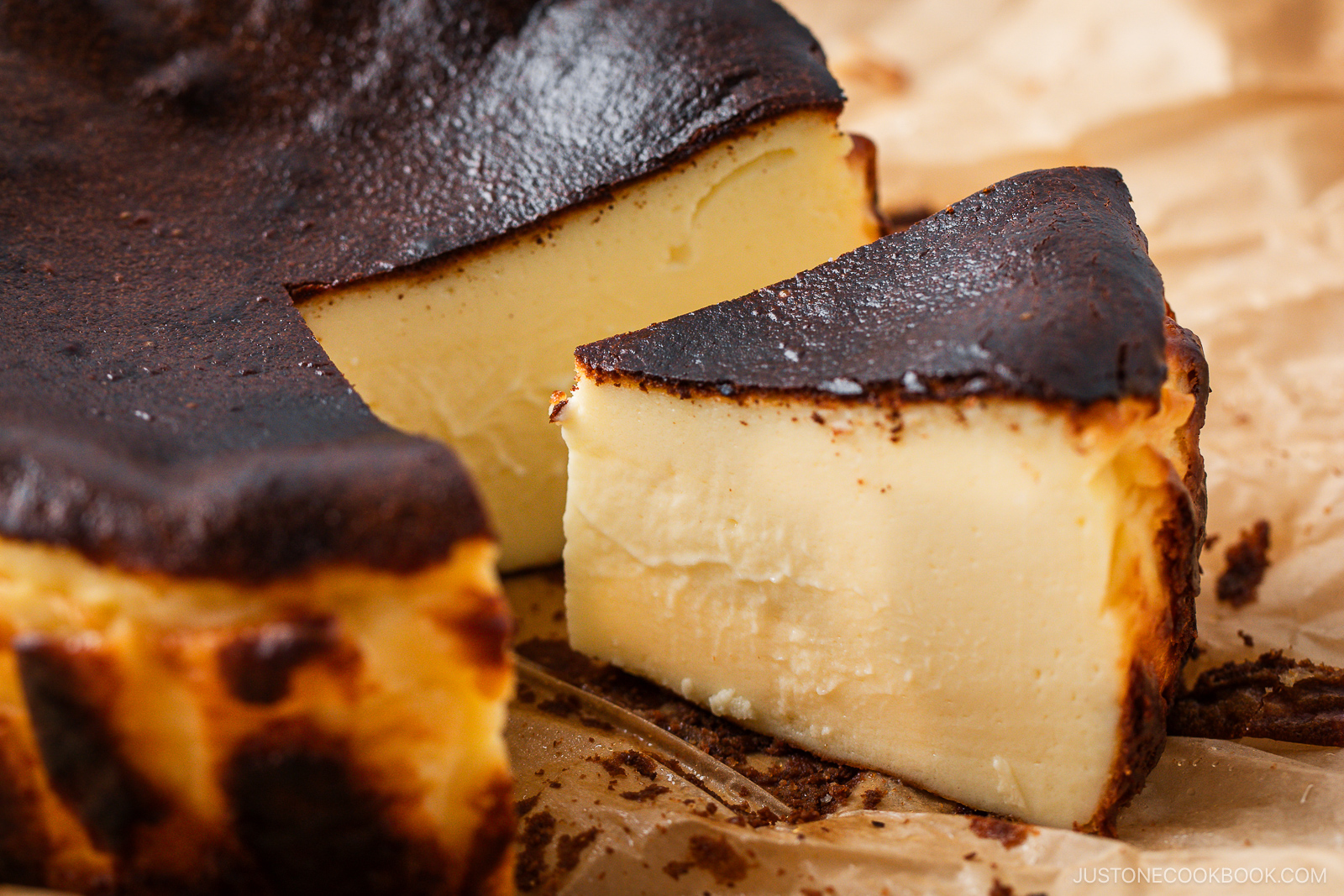 A close-up of a sliced Basque burnt cheesecake on parchment paper, showing its creamy interior and dark, caramelized top.